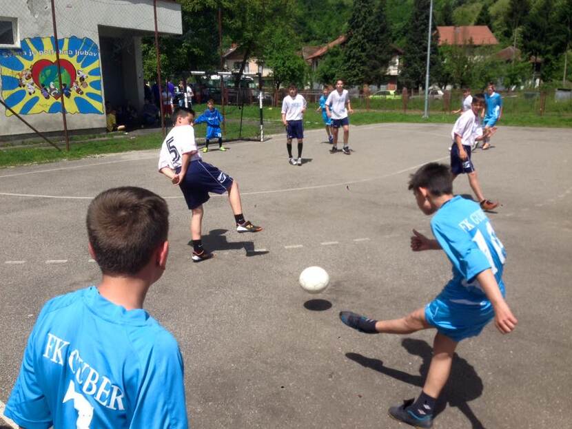 Verhard voetbalveld met spelende kinderen in blauwe shirtjes.