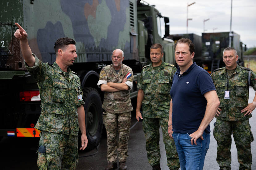 Defensiestaatssecretaris Gijs Tuinman staat tussen een aantal militairen naast een truck en laat zich bijpraten bij de Patriot Task Force in Litouwen.