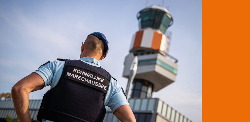 De rug van iemand van de marechaussee, terwijl diegene naar de verkeerstoren op Rotterdam The Hague Airport kijkt.