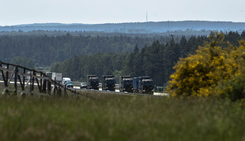 Vier defensievoertuigen achter elkaar op de snelweg in groene, heuvelachtige omgeving.