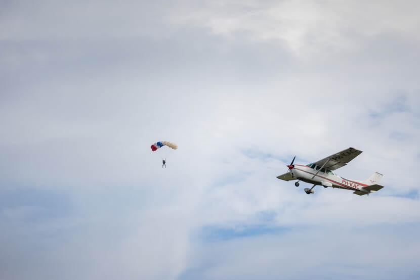 Een vliegtuigje met op de achtergrond een parachutist.