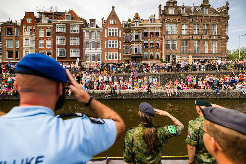 Militairen, op de rug gezien, brengen een groet aan het publiek op de kade tijdens Pride.