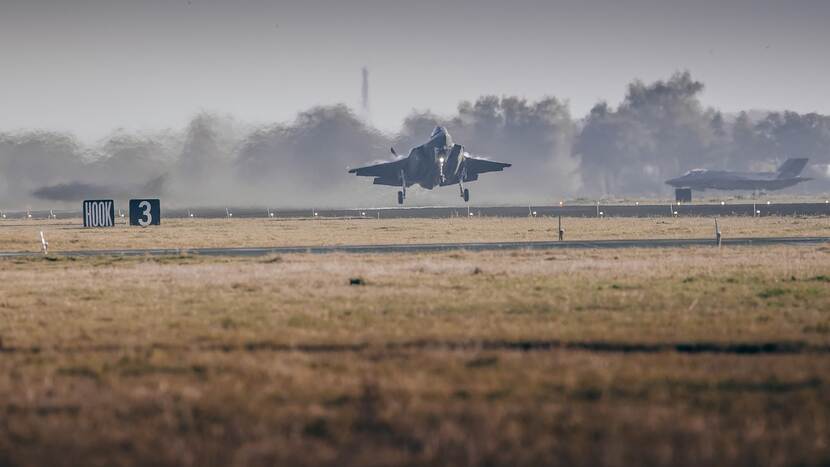 Een F-35 jachtvliegtuig stijgt op vanaf vliegbasis Leeuwarden. Op de voorgrond is gras.