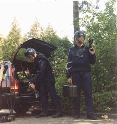 2 militairen met helm op halen spullen uit achterbak rode auto.