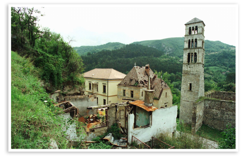 Een kapotgeschoten kerk met daaromheen eveneens vernielde huizen, tussen de bergen.