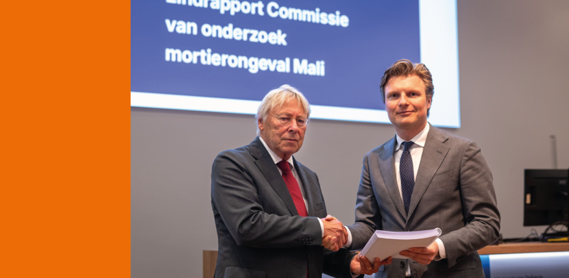 2 heren in kostuum waarbij de een papierwerk overhandigt aan de ander.