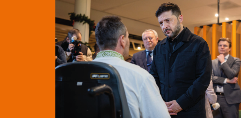 Man met baard staat te midden van een drietal anderen iemand in een rolstoel te woord.