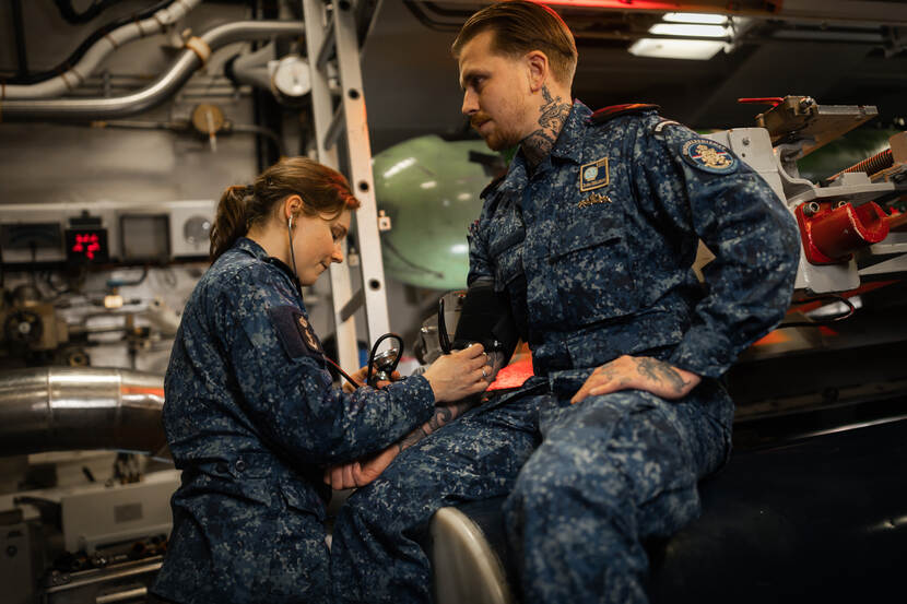Korporaal en verpleegkundige Jeanine meet in de torpedokamer van de onderzeeboot de bloeddruk van een collega.