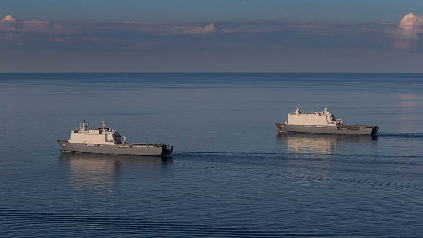 Twee grote marineschepen varen vlak naast elkaar door een glad zeeoppervlak.