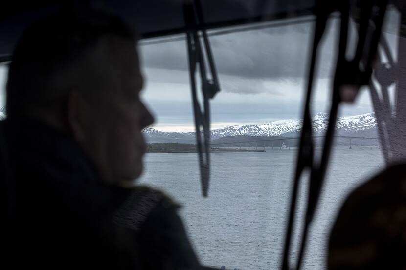 Silhouet van commandeur Lenssen die vanaf de brug van een marineschip naar buiten kijkt.