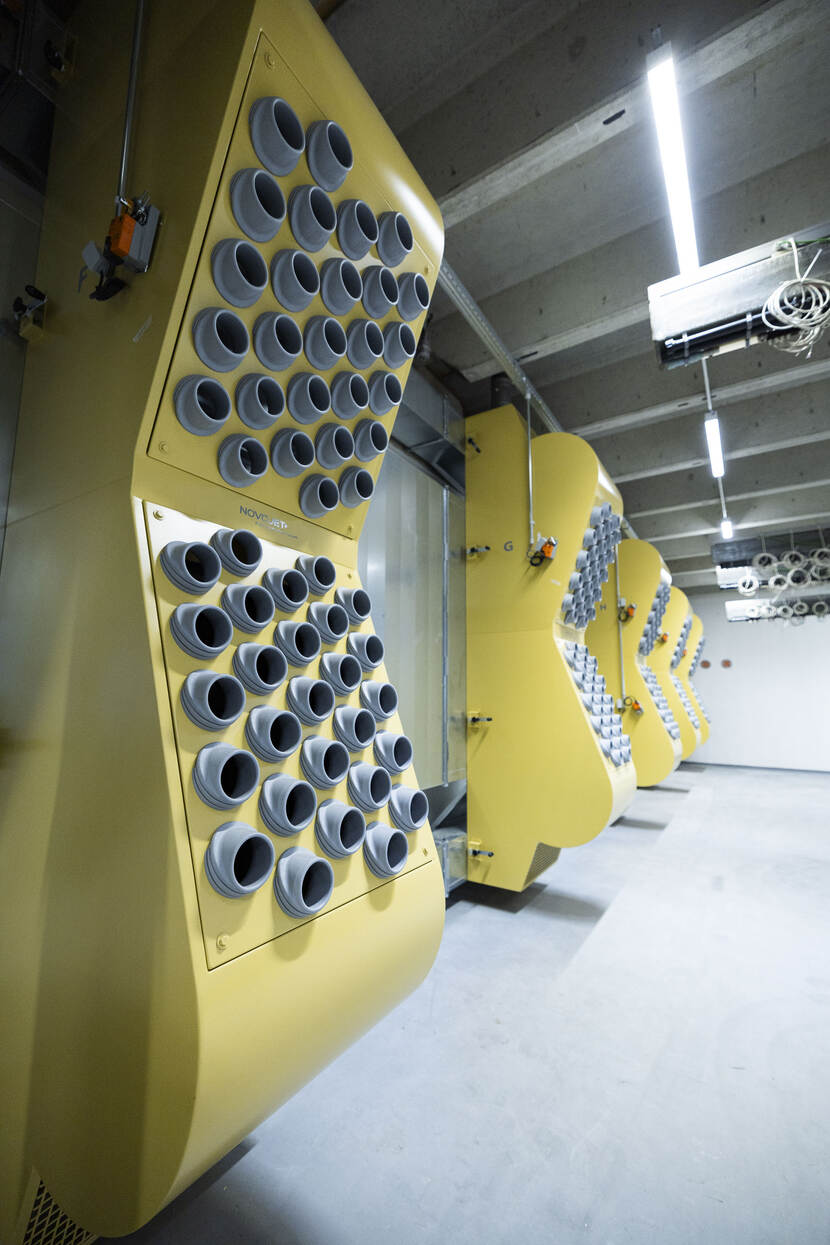 het ventilatiesysteem, dat bestaat uit meerdere gele ombouwen aan de wand, met daarin een groot aantal ronde zuigmonden.