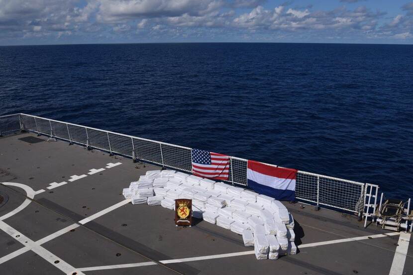 Een stapel drugs op het dek van een marineschip, met daarbij de Nederlandse en Amerikaanse vlag.