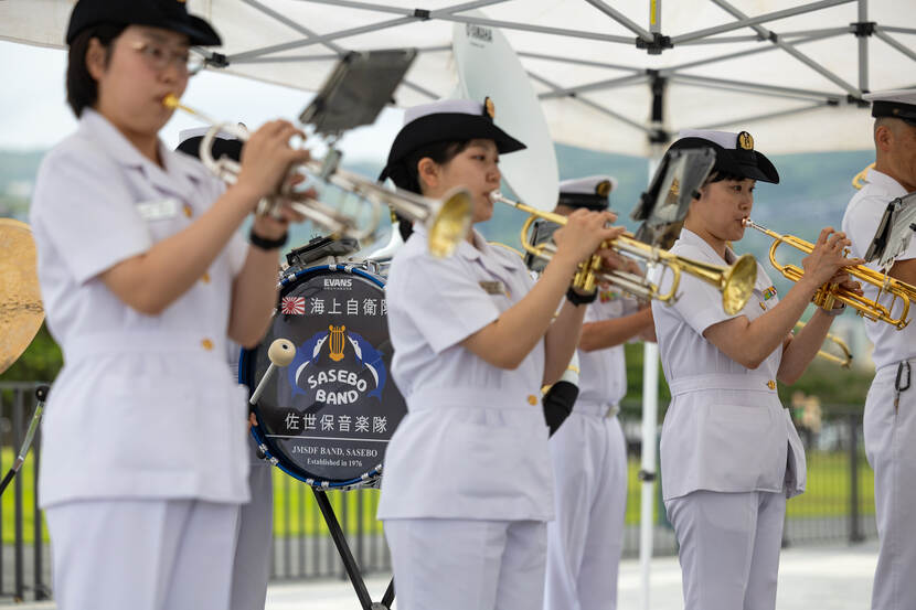 Drie vrouwelijke trompetspelers in wit uniform.