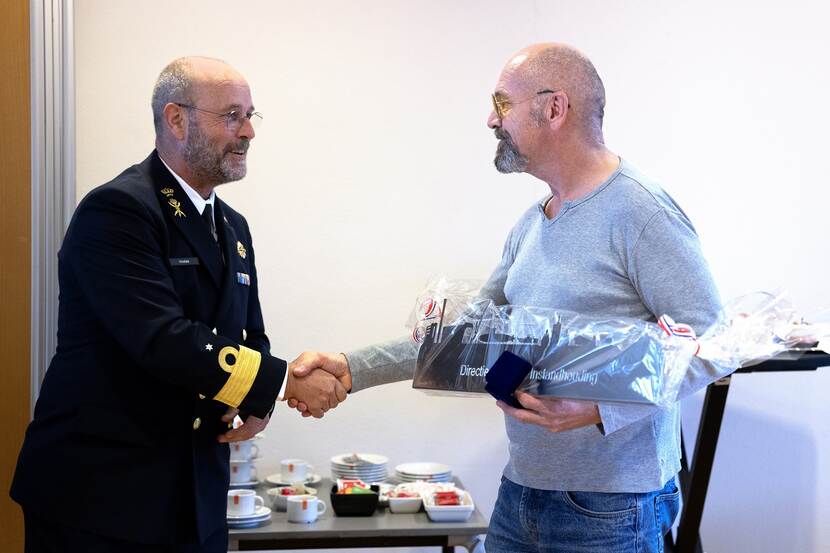 Henk Okkerse schudt de hand van commandeur Jeroen Hodes, met een ingepakt presentje in de hand.