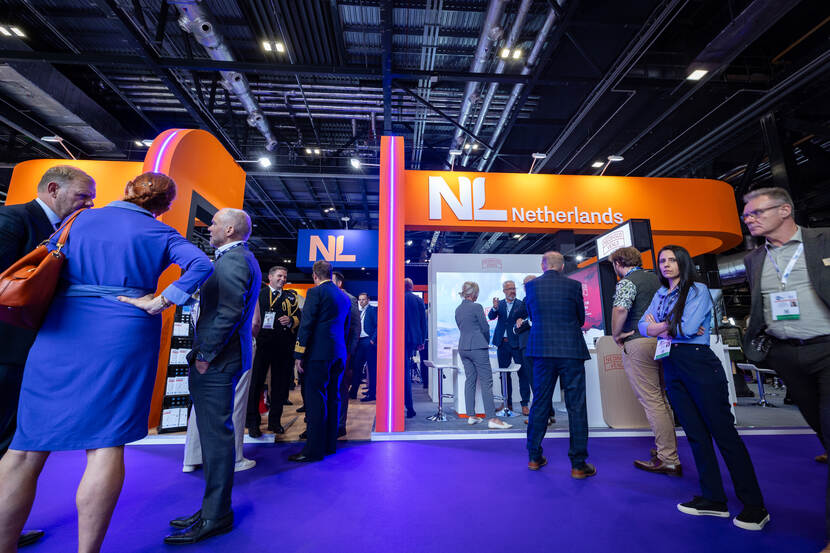 De druk bezochte Nederlandse beursstand. Mensen in zakelijke kleding staan te praten of lopen langs.