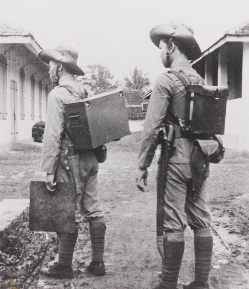 Twee KNIL-militairen met op hun rug een telegrafieset.
