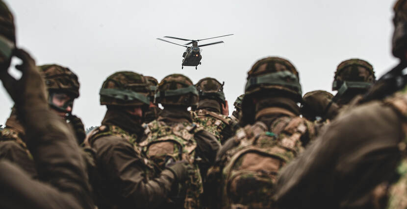 Landmachters te velde met in de lucht een Chinook-transporthelikopter.