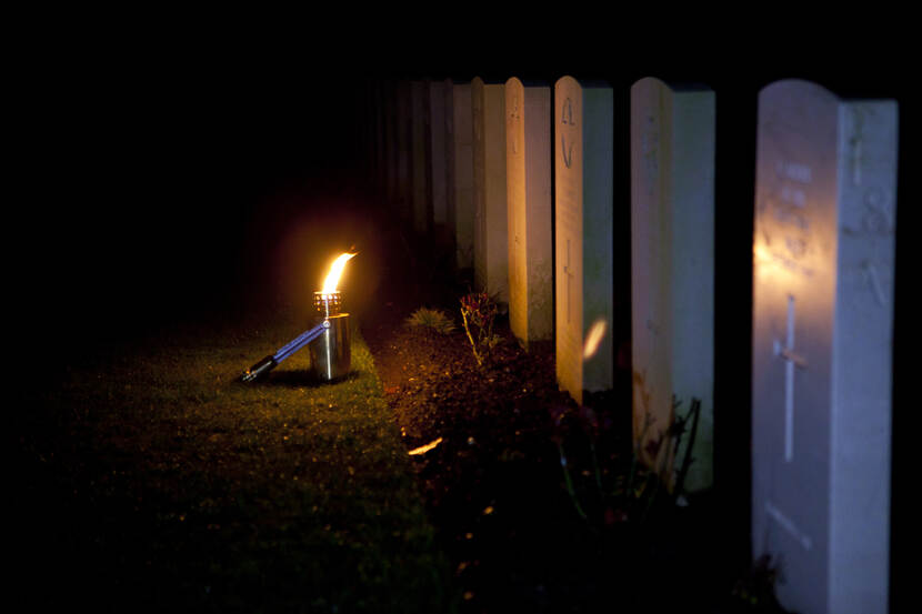 Foto van de oorlogsgraven in Oosterbeek, in de avond met een fakkeltje.