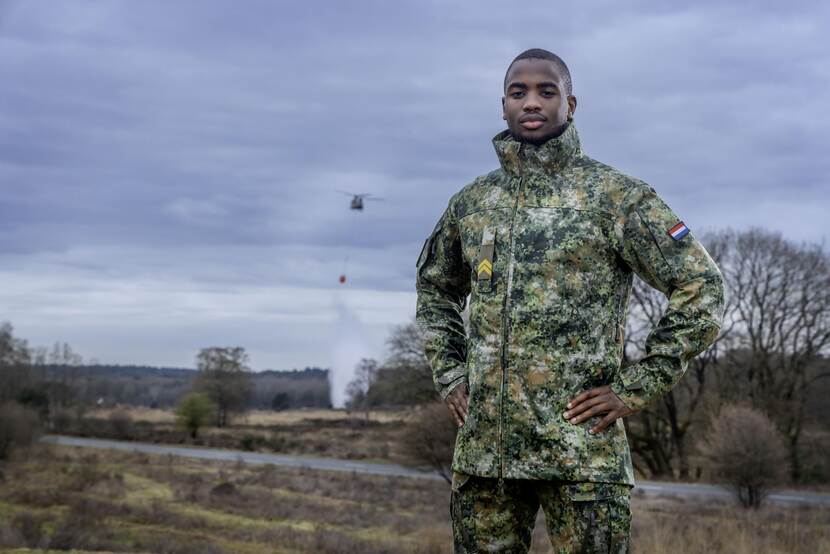 Een militair toont het nieuwe tenue terwijl in de achtergrond een Chinook vliegt.