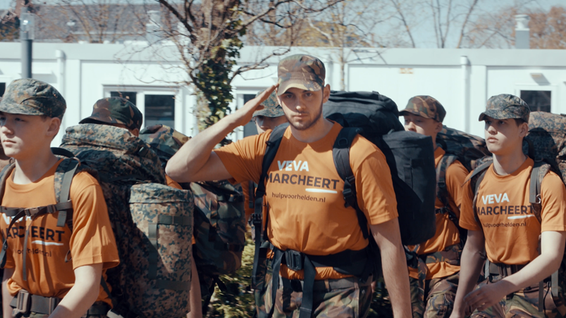 Een militair brengt een eregroet, terwijl hij langsmarcheert in oranje t-shirt.