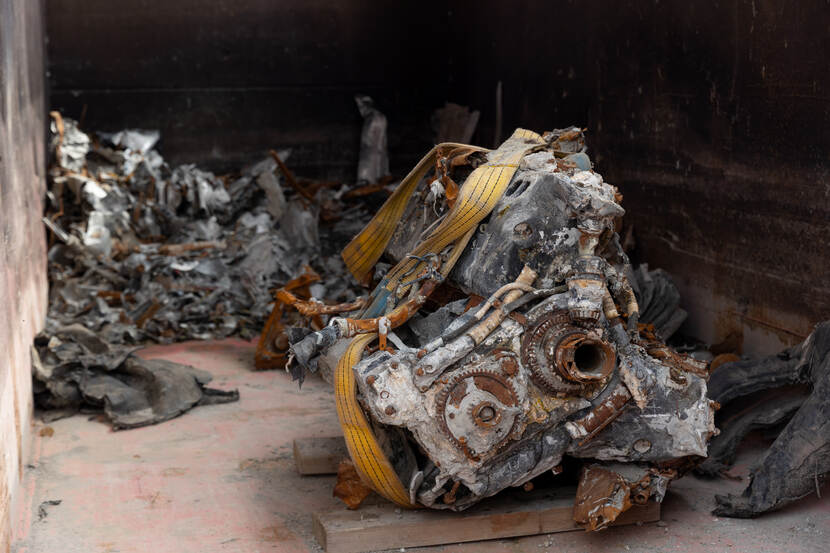 Een container met daarin delen van een vliegtuig. Voorin het beeld een deel van een verwrongen motorblok.