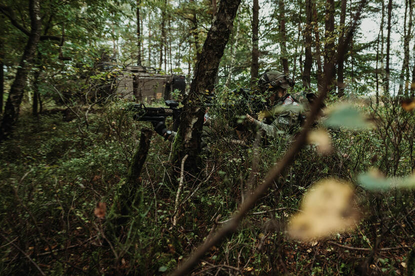 Een militair schiet met zijn wapen in de bosschages.