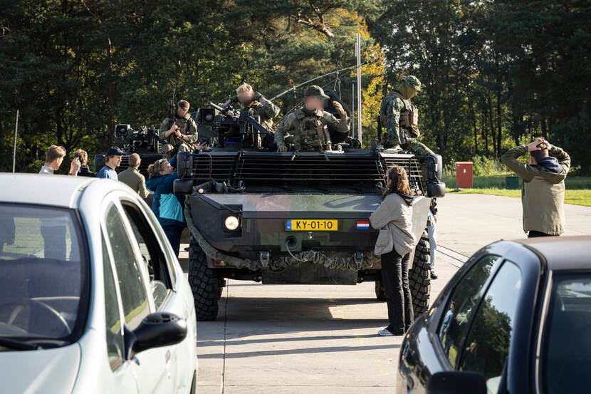 Verschillende burgers drommen rond de verkenningsvoertuigen op de fictieve snelweg.