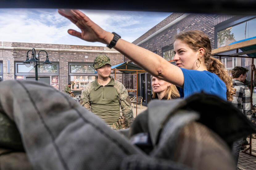 Een militair staat naast de Fennek en spreekt twee actrices toe.