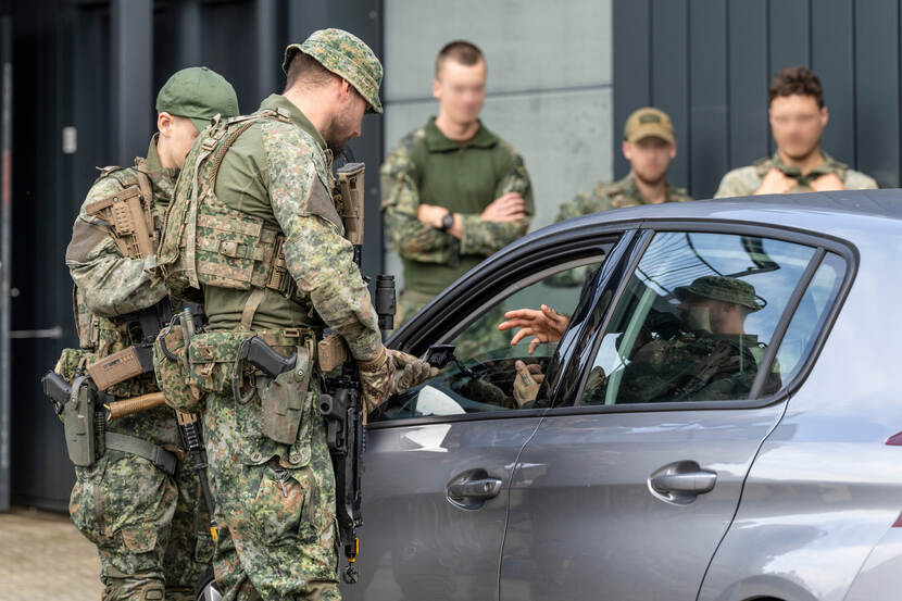 Militairen spreken met een bestuurder van een geparkeerde auto door het geopende raam aan de chauffeurszijde.