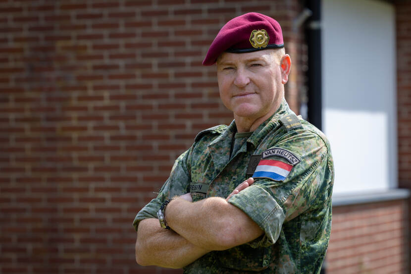 Militair met rode baret kijkt in de camera met armen over elkaar.