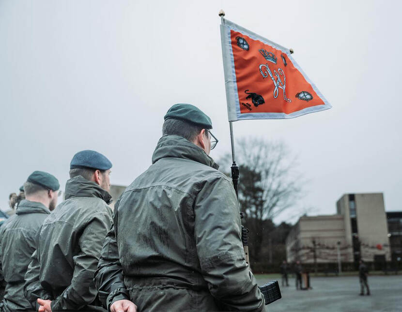 Drie militairen op de rug gezien met een compagnie vlag