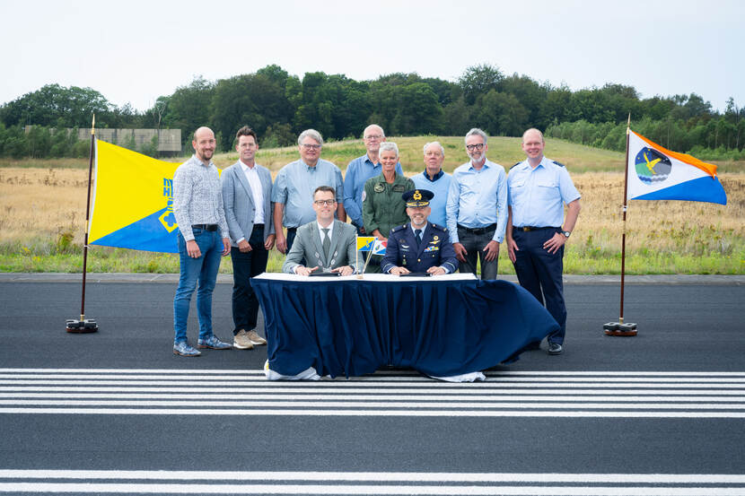 Een groep mensen staat bij een tafel met aan weerszijden vlaggen.