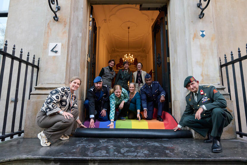 Militairen en burgermedewerkers rollen samen een regenboogloper uit.