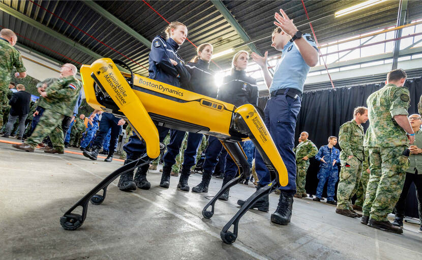 Een gele robothond met daaromheen pratende mensen.