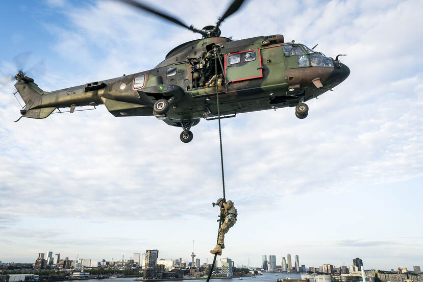 En militair daalt via een fastrope af uit een Cougar. Op de achtergrond de Rotterdamse skyline.
