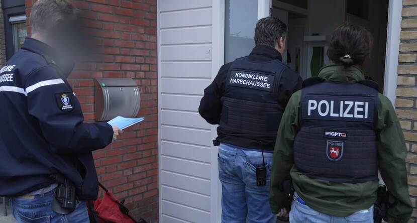 Een marechaussee en een Duitse collega staan voor de deur van een woning.