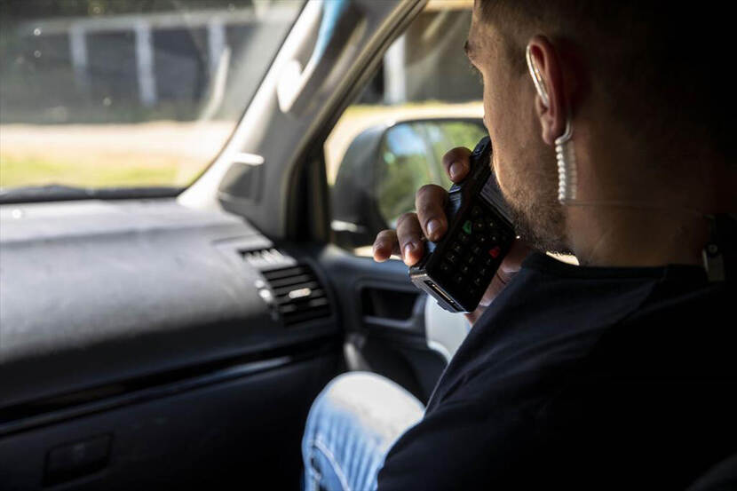 Een persoonsbeveiliger praat in zijn portofoon terwijl hij in de auto zit.