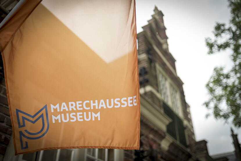 Een vlag van het Marechausseemuseum met op de achtergrond het museum.