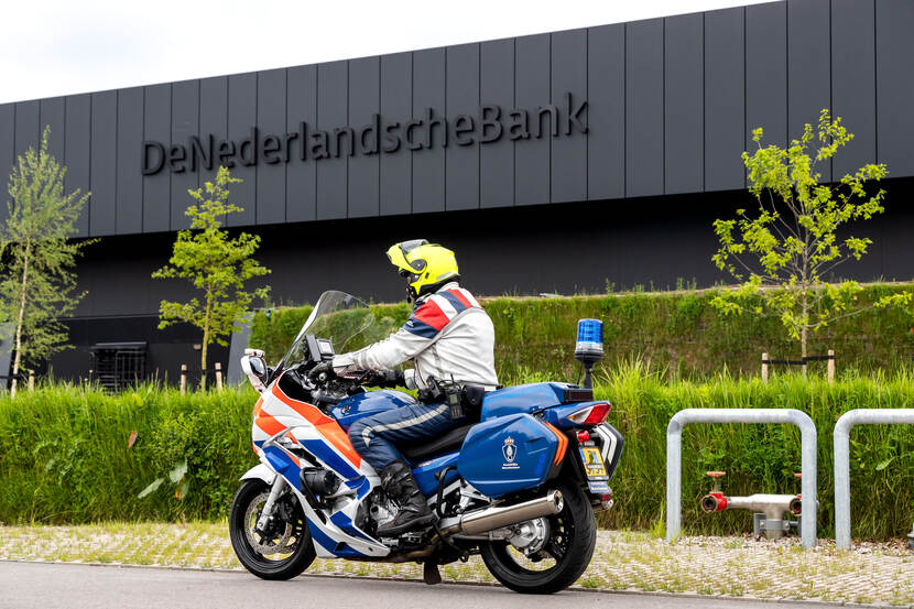 Een afbeelding van een motorrijder met het gebouw van De Nederlandsche Bank op de achtergrond.
