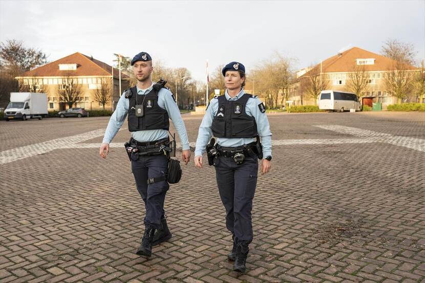 Twee marechaussees, man en vrouw, in blauw tenue lopen in nieuwe veiligheidvest. (kop)