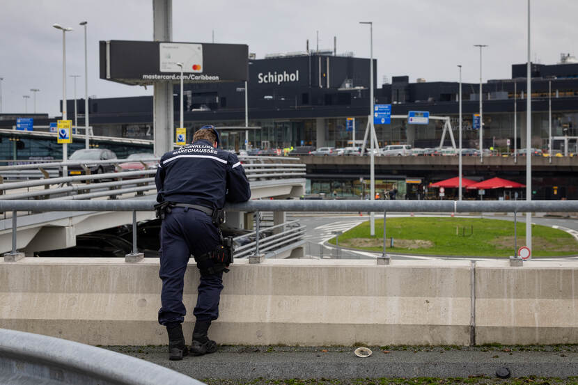 Marechaussee kijkt over de reling van parkeerdek op Schiphol.