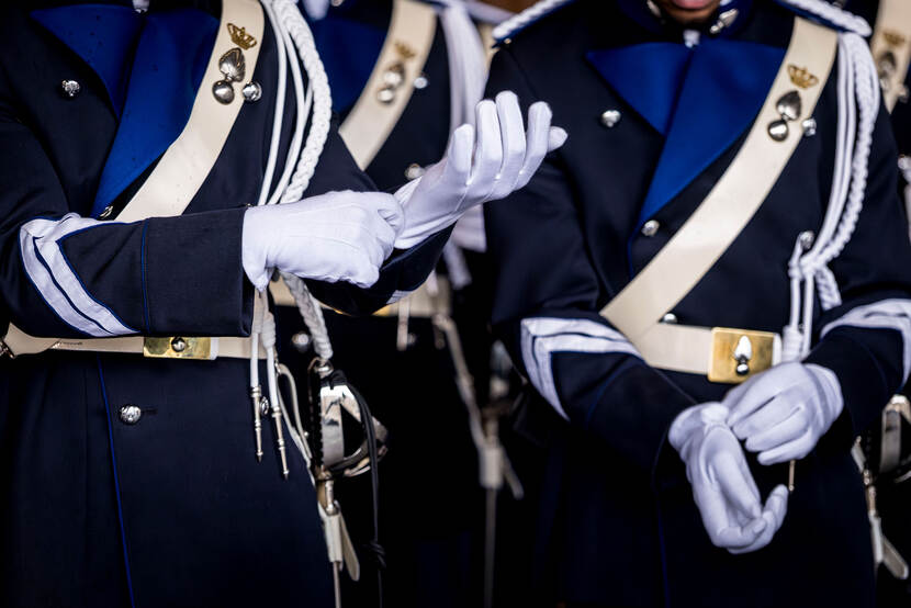 Een close-up van een marechaussee die z’n witte handschoenen aantrekt.
