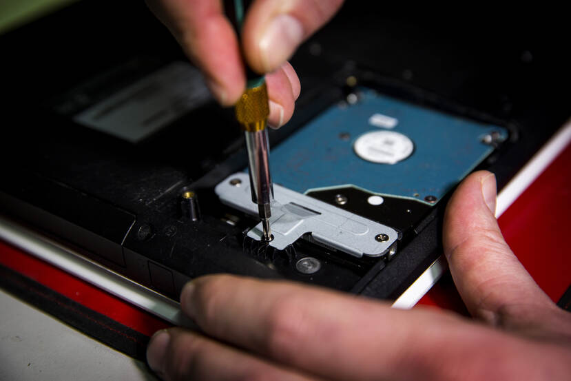 Hand met kleine schroevendraaier monteert een harde schijf in een laptop.