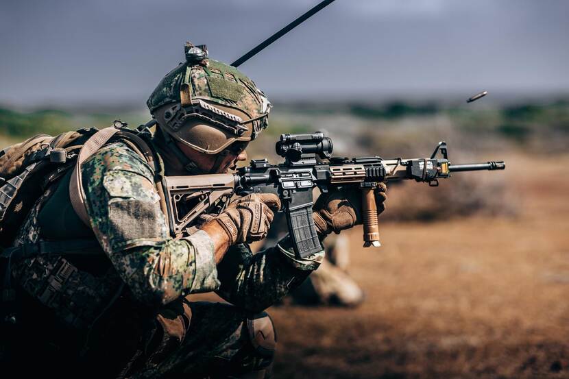 Een militair schiet in staande houding met zijn Colt, waar een patroon uit vliegt.