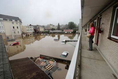 Een vrouw op een galerijflat met beneden een overstroomde parkeerplaats. Auto's staan tot aan hun dak in het water.
