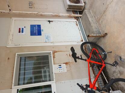 De witte deur met daarop een Nederlandse vlag van het kantoor van Mandy. Voor de deur staat een rode fiets.