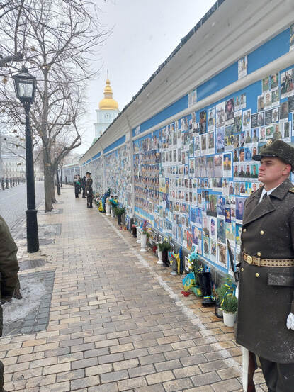 Een Oekraïense soldaat houdt de wacht bij de muur vol met foto's van gesneuvelde militairen.