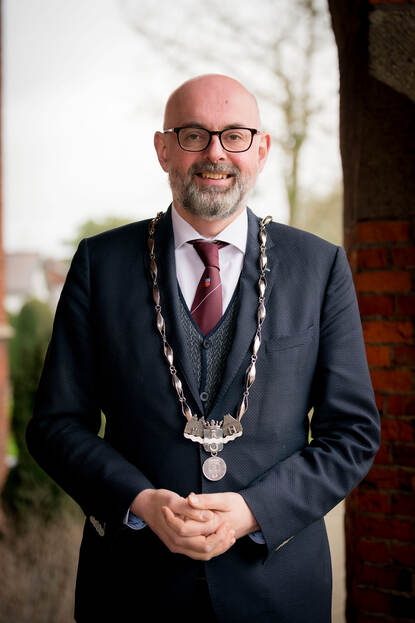 Staande foto van burgemeester Martijn Vroom met z’n ambtsketen om, voor het gemeentehuis van Leidschendam-Voorburg.