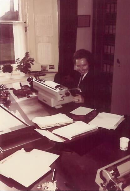 Een sepiakleurige foto van Judith Dalmeijer achter een bureau, tikt op een typemachine.