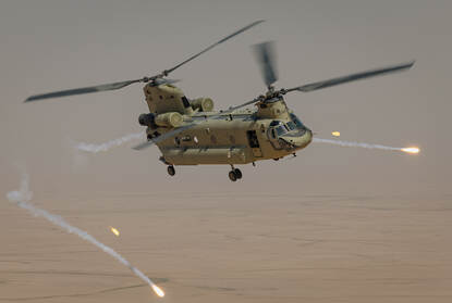 Een Chinook in de lucht boven Irak, met flares om zich heen